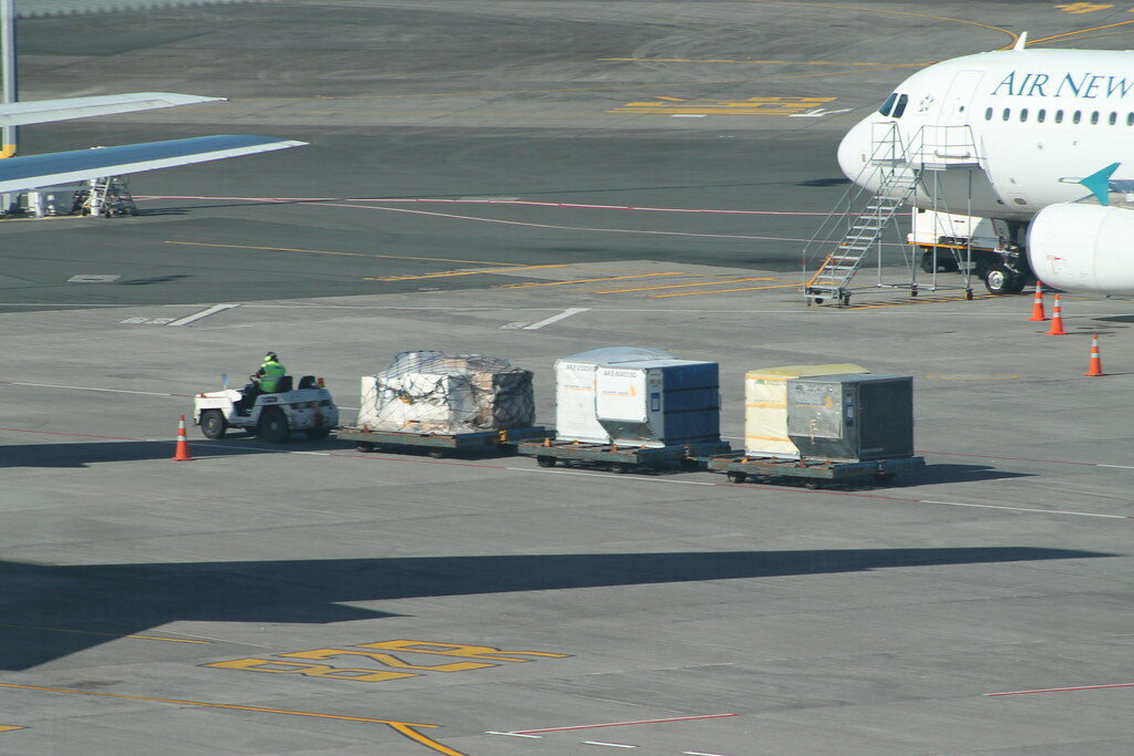 Air cargo ULD containers on dollies being towed across an airport apron by a ground tug