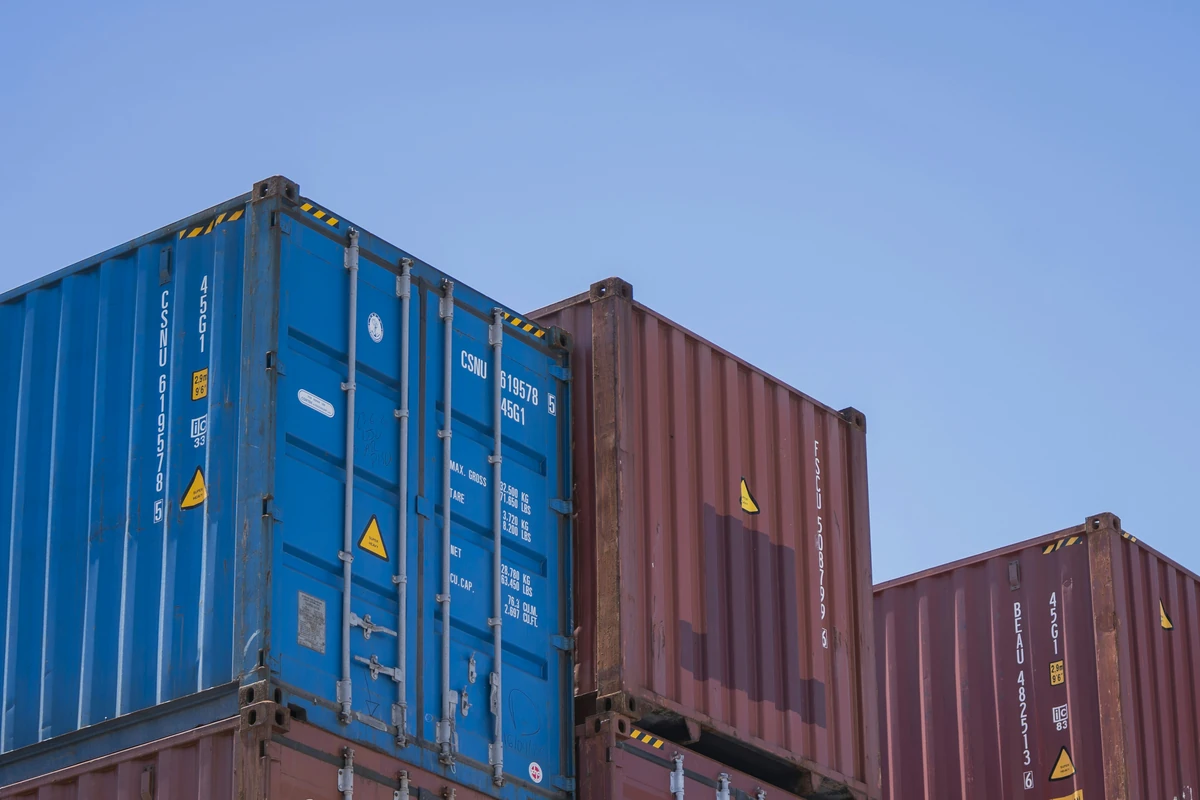 Low-angle view of stacked blue and rust-red shipping containers against a clear blue sky