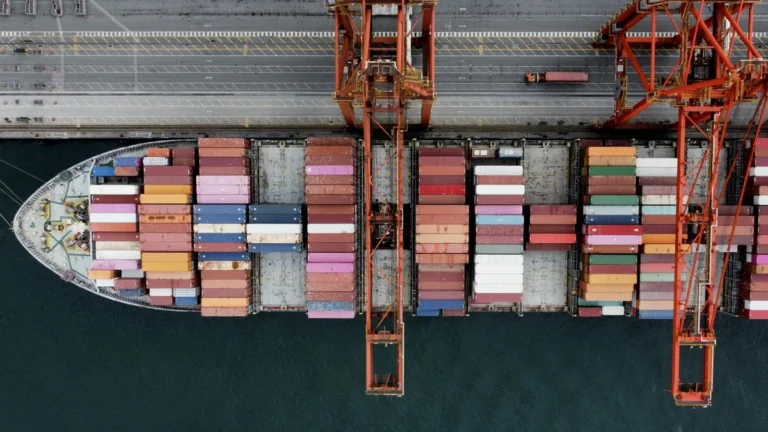Overhead view of a container ship moored at a quay beside two red gantry cranes and a terminal road