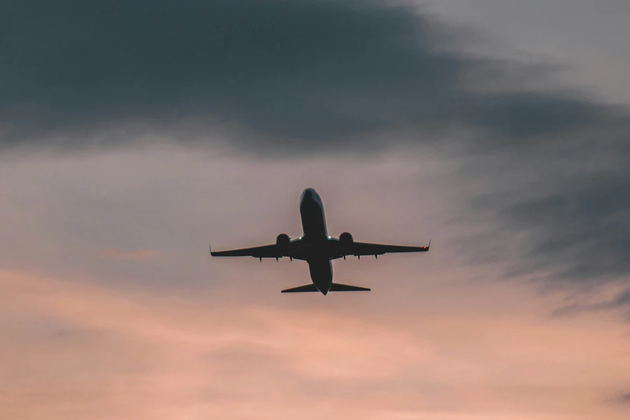 Silhouette of a twin-engine jet climbing into a cloudy pink and grey sky at dusk