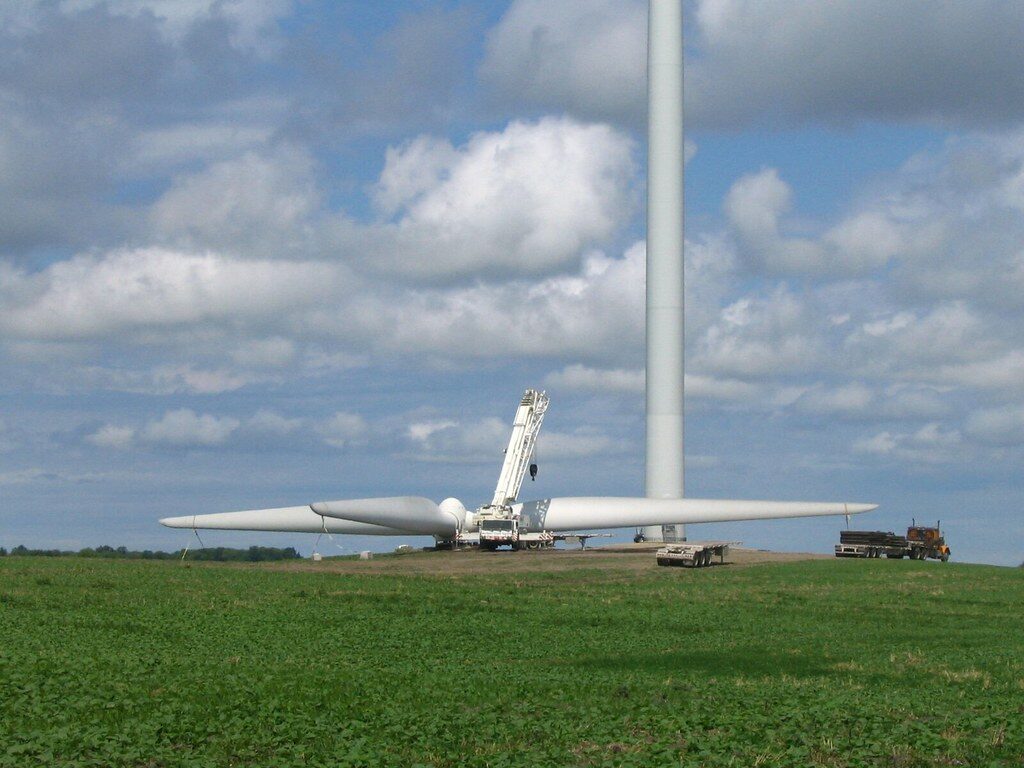 Wind turbine tower and rotor assembly laid out in a field beside a mobile crane and flatbed trailers