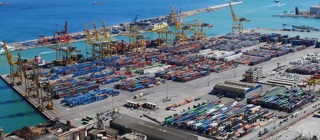 Aerial view of a busy container terminal with stacked containers, gantry cranes and a ship at berth