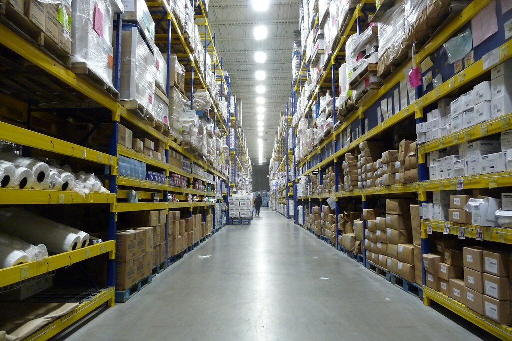 Warehouse aisle lined with tall yellow pallet racking holding wrapped and boxed stock